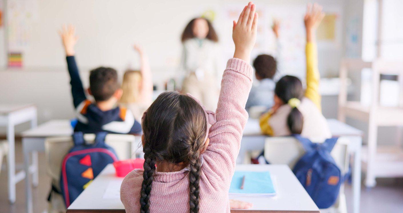 Education, Raised Hand And Girl Student In Classroom With Teacher For Learning, Discussion And Knowledge. Help, Studying And Children Students With Questions For Female Educator Or Tutor At School. Students raising hands in a classroom